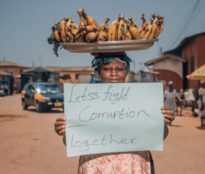 A woman balances bananas on her head and holds up a sign in favor of fighting corruption